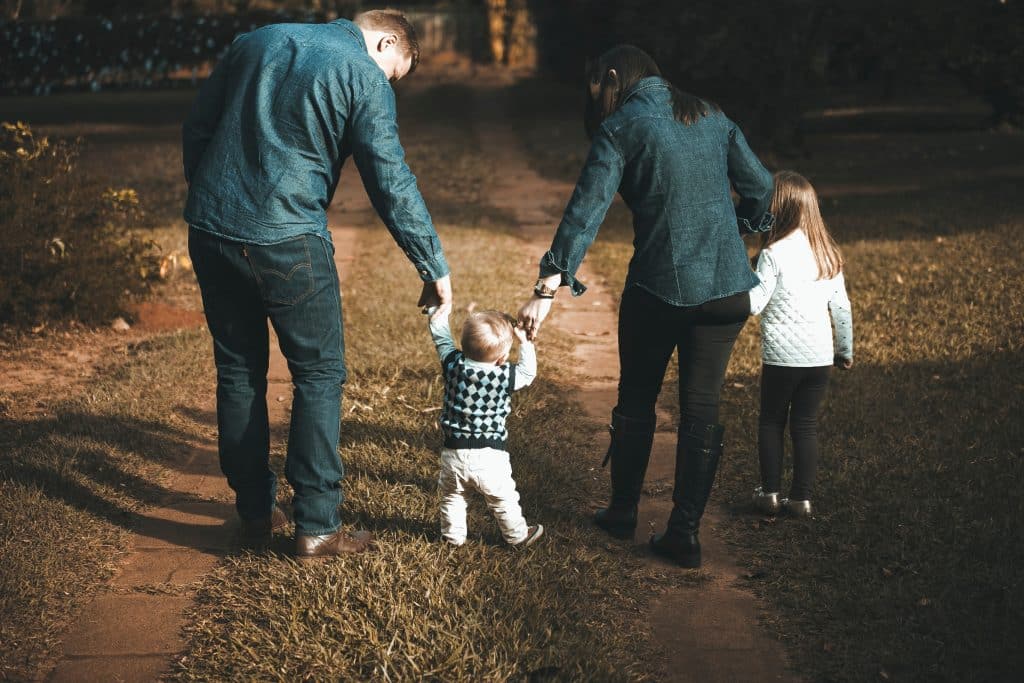 a family with a mother, father and two young children seen walking from behind.