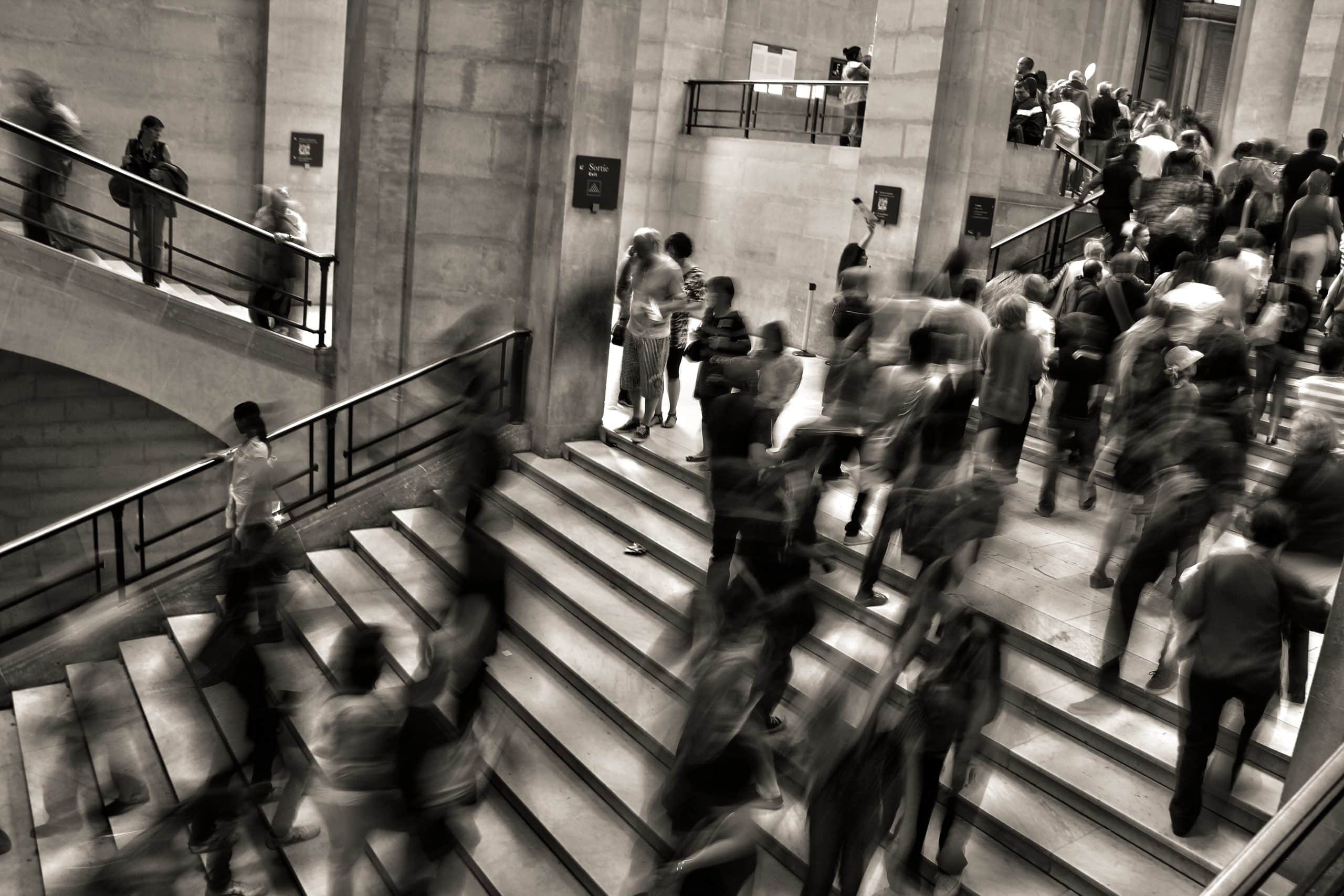 a blurred photo of a crowd of people navigating a stairway in a large office building