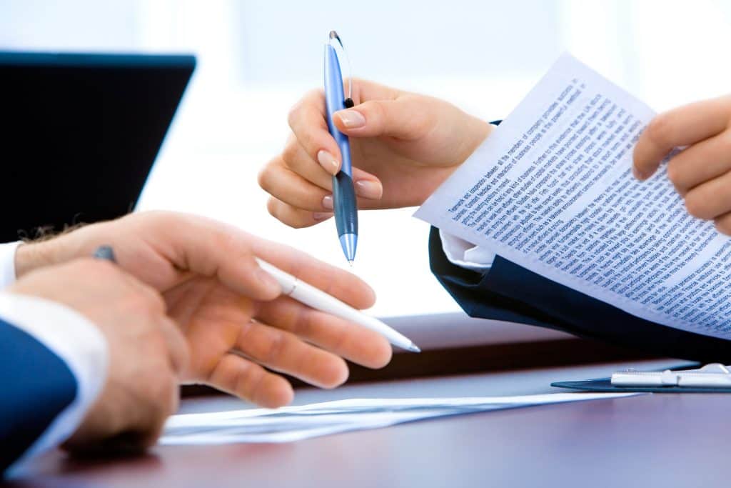 close up of two sets of hands holding pens and reviewing contract over a desk