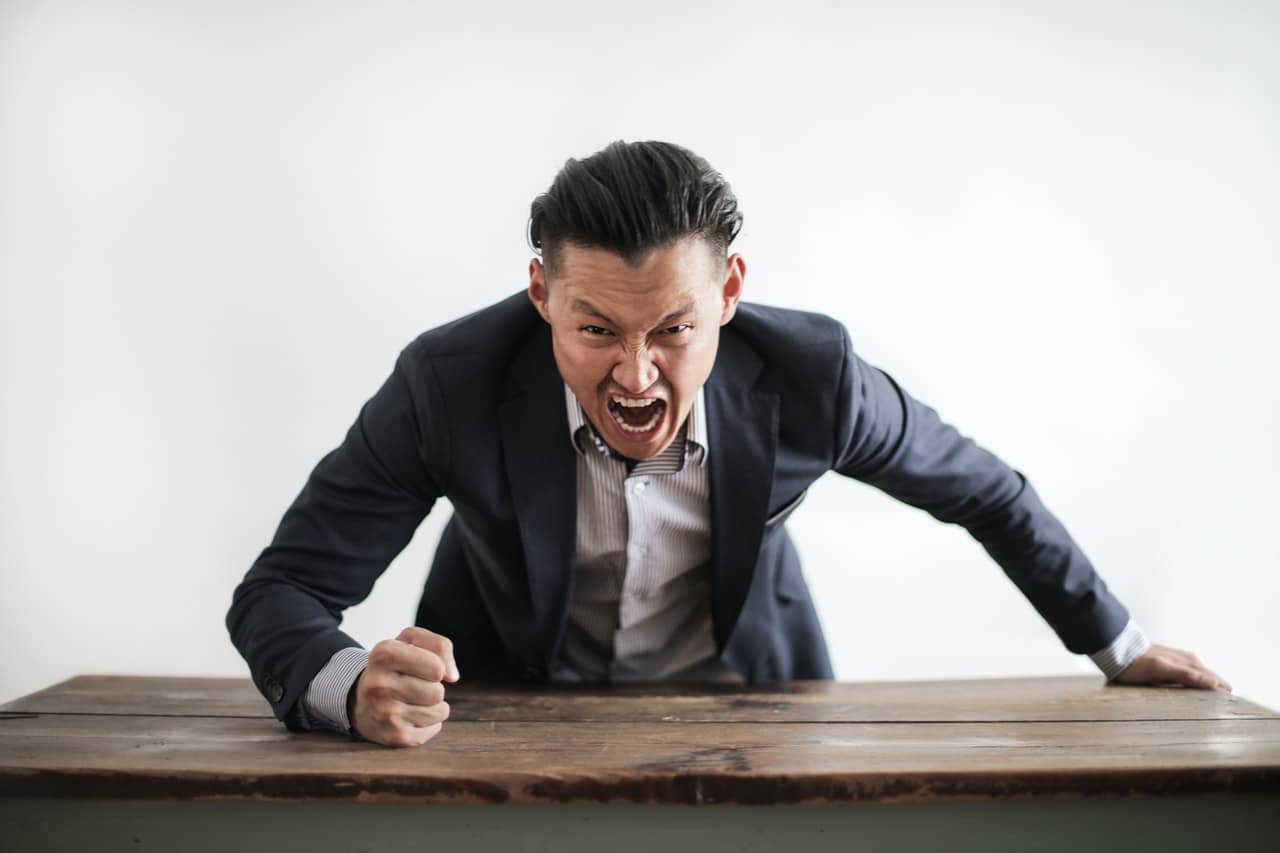 A man banging his fist on a desk and yelling, representing violence and harassment at work