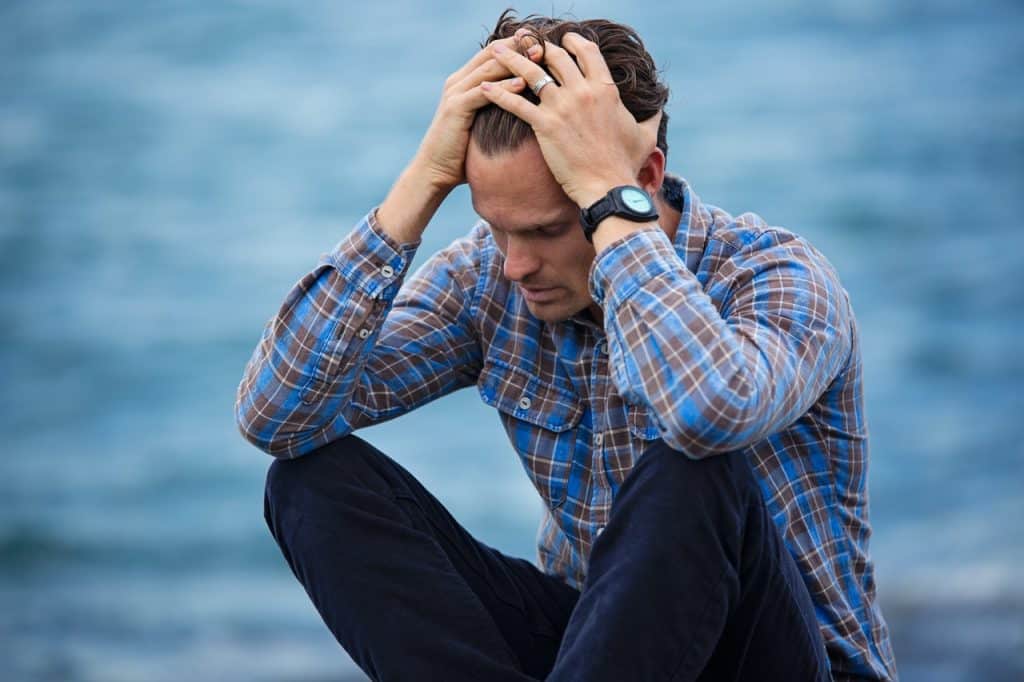 Man with his head in his hands sitting by the water representing someone who has been laid off