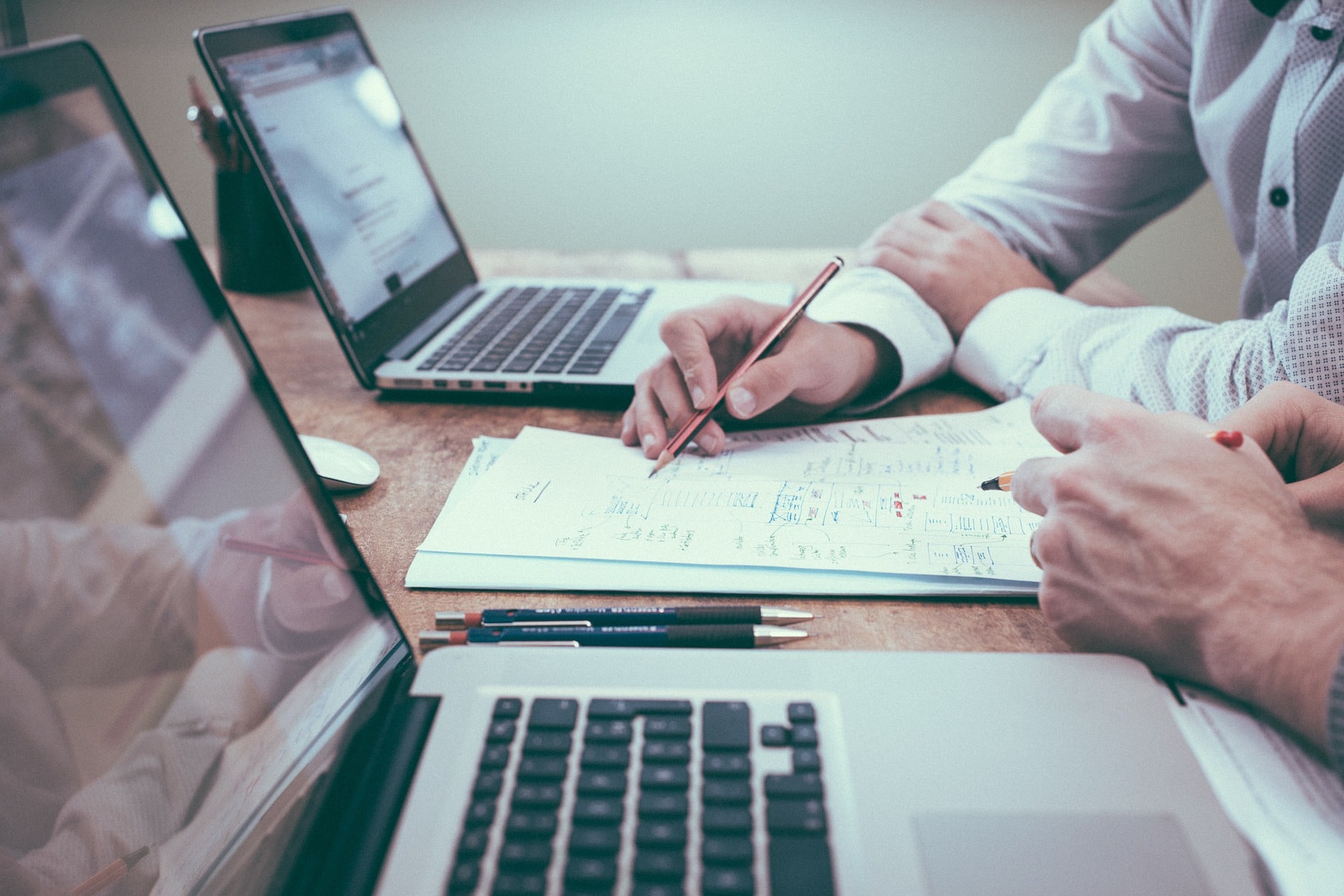 the hands of two people who appear to be negotiating terms of a contract with laptops on a table in front of them