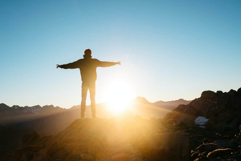 A man standing on a hill with arms spread while the rises, representing a possible return to work after COVID closures