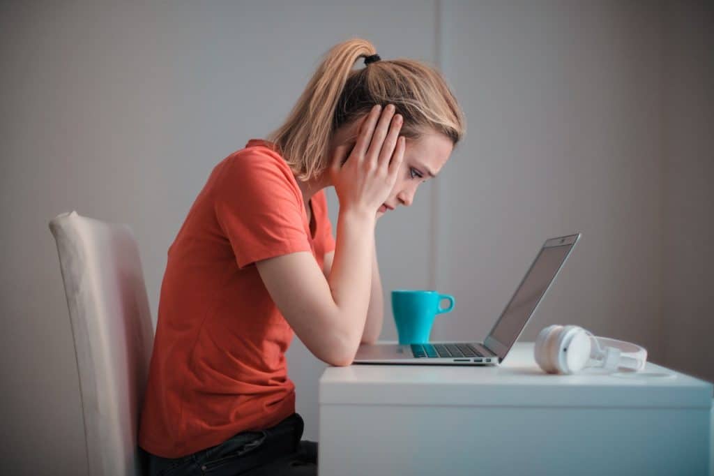 A woman in distress looking at her computer representing a poisoned work environment