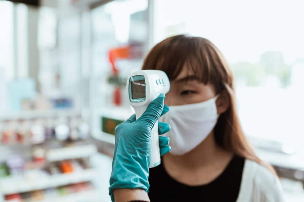 A woman in a mask has her temperature taken representing workplace health policies in light of COVID