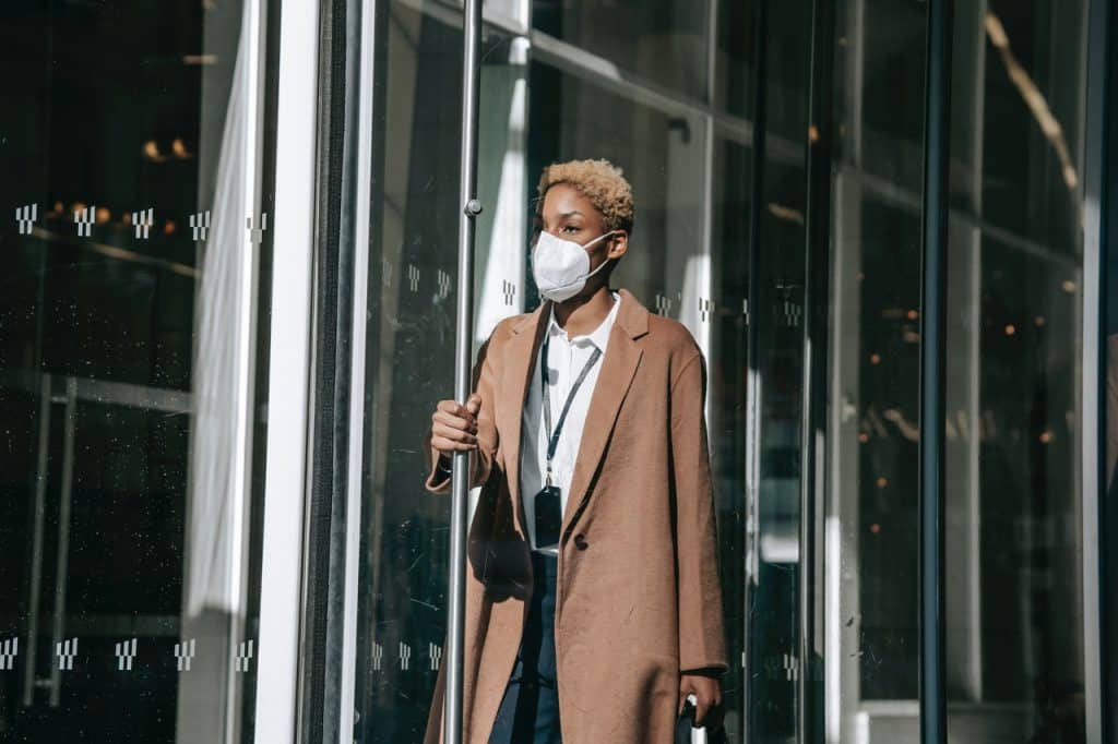 A woman wearing a face mask leaving an office building representing possible implications of COVID-19 on termination notice periods