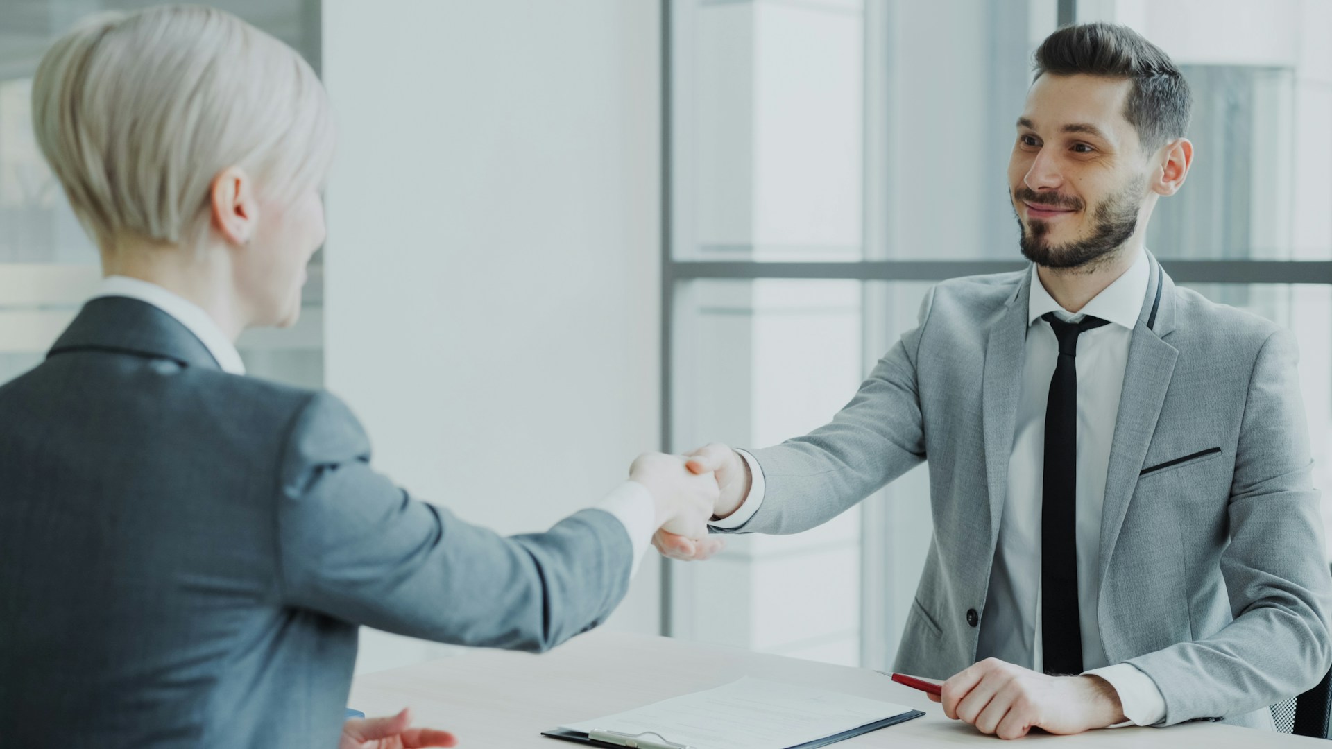 A man and woman, facing each other across a desk, shake hands over an employment agreement, representing red flags in Ontario employment agreements