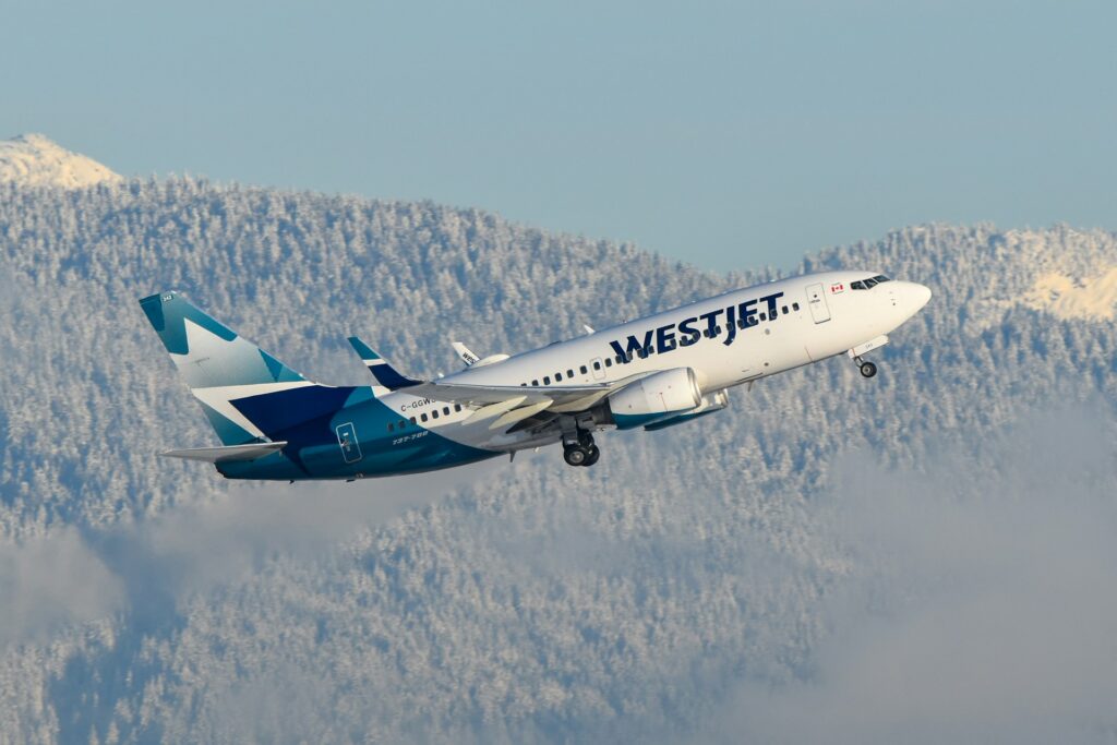 A WestJet plane flying over a mountain range, representing the WestJet and CUPE dispute and strike in 2026.