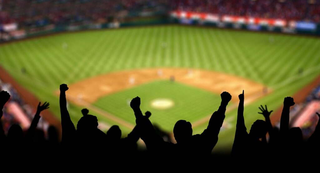 Excited fans at a baseball stadium lifting their hands and arms, representing workplace gambling, betting pools and fantasy sports.